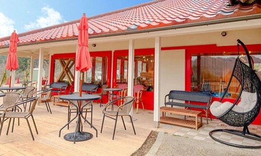 赤い屋根のカフェのウッドデッキテラス。赤いパラソルのテーブル席と吊り椅子が並ぶ