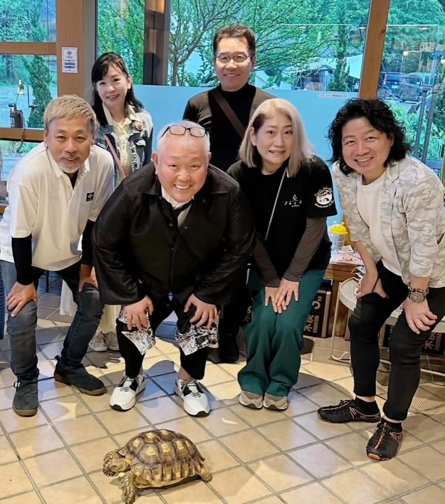 いぶきヴィレッジのカフェで、キャスト・スタッフのみなさんと並ぶ江原啓之さん。足元をリクガメが歩いている。