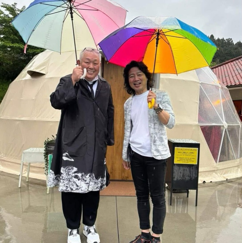 雨の日、グランピングドームの前で傘をさして並ぶ2人