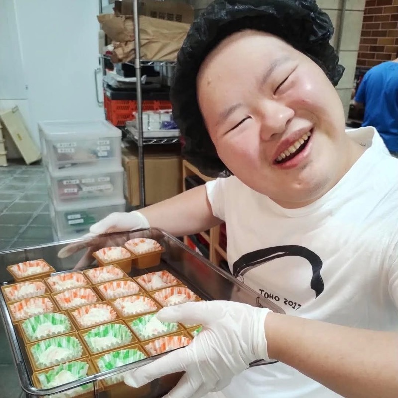 厨房で仕上げた料理のトレイを持ち、笑顔を見せるキャスト